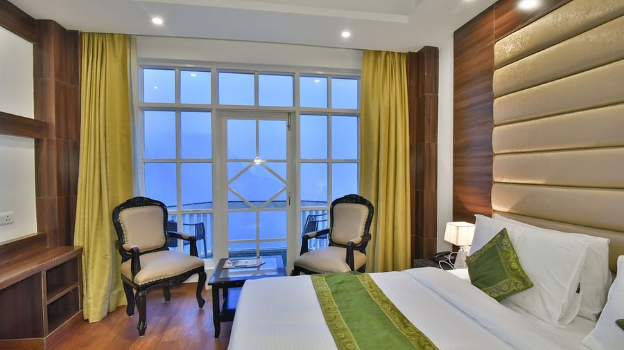 A large bed next to two chairs placed near a large window in the Premium Room at DLS Highland Resort and Spa, Mussoorie.